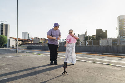 Brother and sister dancing and filming video through smart phone on street