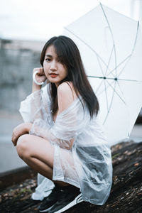 Portrait of young woman with umbrella sitting outdoors