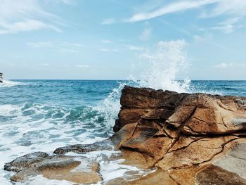 Waves splashing on rocks by sea against sky