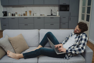 Young woman using laptop while sitting on sofa at home