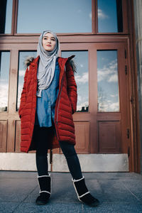 Full length of young woman standing against entrance door in city