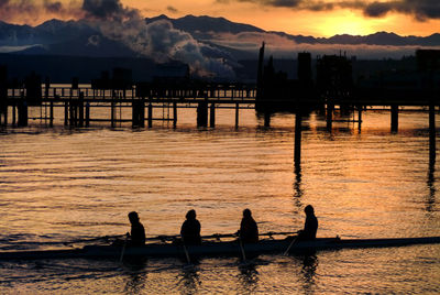 Silhouette people on riverbank against sky during sunset