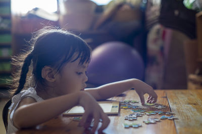 Cute girl playing with jigsaw puzzle on table at home