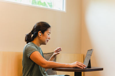 Side view of young woman using laptop at home