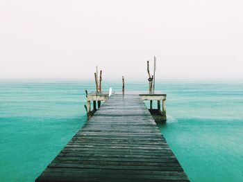 Wooden pier on calm sea against clear sky