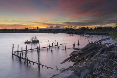 Wooden posts in lake against sky during sunset