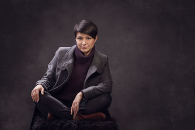 Portrait of young man sitting against black background