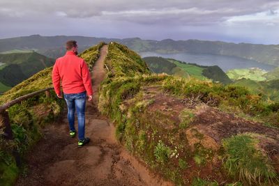 Rear view of man walking on mountain against sky