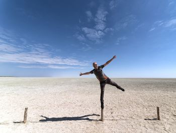 Man balancing on wooden post in desert against blue sky