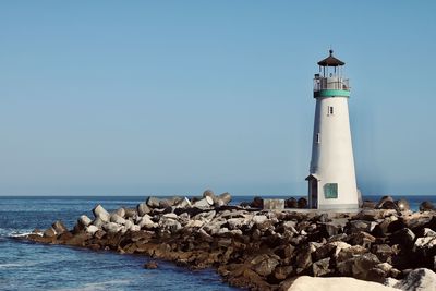 Lighthouse by sea against clear sky