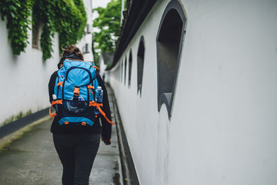 Rear view of woman walking on street by wall