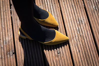 Low section of woman wearing yellow shoes on boardwalk