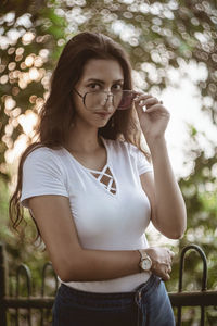 Portrait of young woman wearing eyeglasses while standing against trees