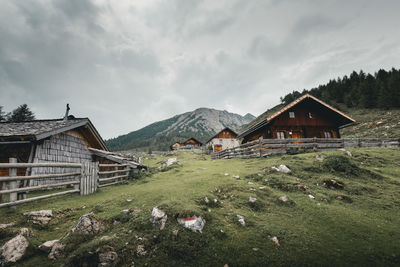 House on field by houses against sky