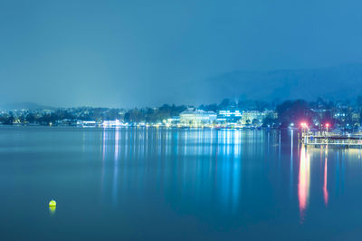 Reflection of illuminated city on lake against clear sky during night