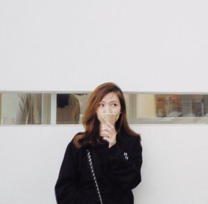 Young woman looking away while standing against wall