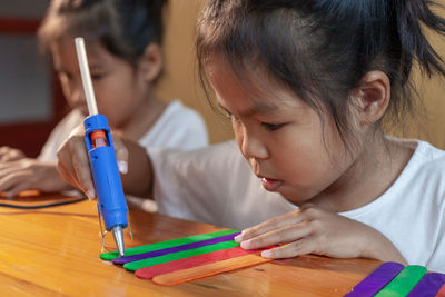 Close-up of sisters making craft on table at home