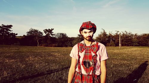 Portrait of young man standing on field against sky
