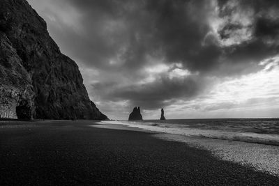 Scenic view of rocky mountain at beach against cloudy sky