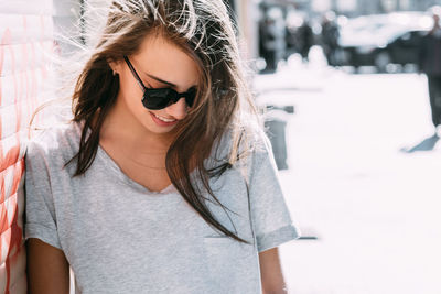 Smiling young woman in sunglasses standing on sidewalk during sunny day