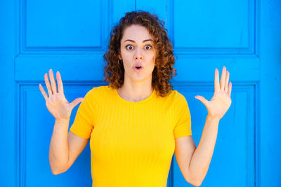 Portrait of young woman gesturing against blue wall