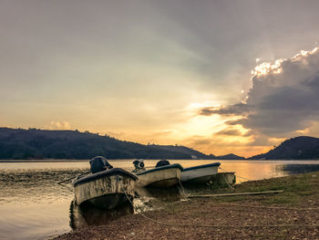 Boats moored on shore against sky during sunset