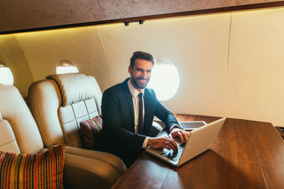 Smiling businessman using laptop in airplane