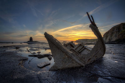 Driftwood on beach against sky during sunset