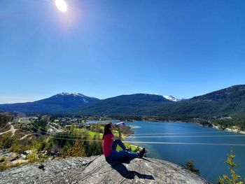 Man sitting on mountain by lake against clear blue sky