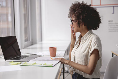 Young woman using phone while sitting on table