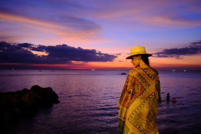 Man standing on rock by sea against sky during sunset