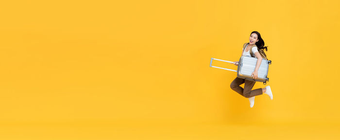 Woman holding umbrella against yellow background