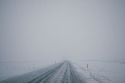 Road amidst snow covered field against sky