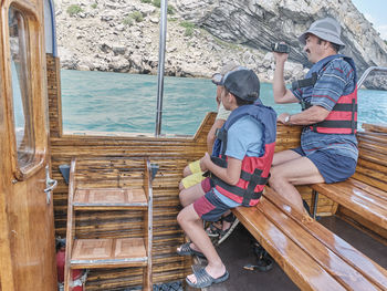 Rear view of men sitting on wood against water