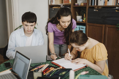 Siblings assisting down syndrome sister while doing homework at home