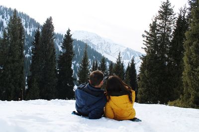 Rear view of couple lying on snow covered mountain against sky