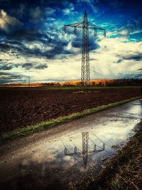 Electricity pylon on field against cloudy sky