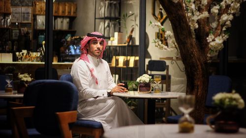 Portrait of young man wearing dish dash sitting on chair in restaurant