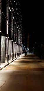 Man walking on illuminated road amidst buildings in city at night