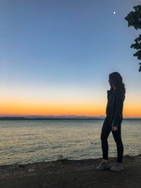 Woman standing at lakeshore against sky during sunset