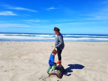 Siblings playing at sandy beach against blue sky