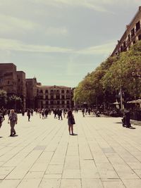 People on sidewalk in city against sky