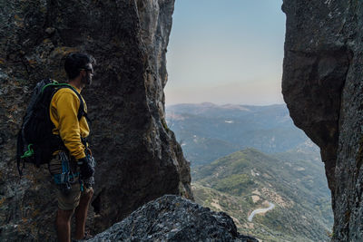 Side view of unrecognizable male explorer with backpack admiring majestic view of mountain ridge while resting on rocky mountaintop