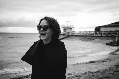 Woman laughing at beach against sky