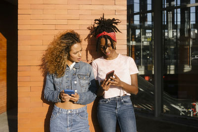 Young woman showing mobile phone to friend on sunny day