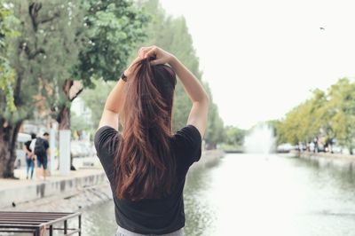 Woman adjusting hair while standing against canal in city