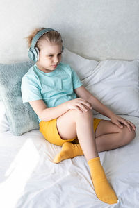 Cute boy listening to music in earphones seating on bed. child wearing headphones listens to music.