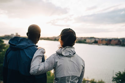 Rear view of male and female athletes looking at sea while standing on hill