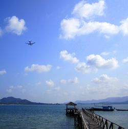 Low angle view of airplane over sea against cloudy sky on sunny day