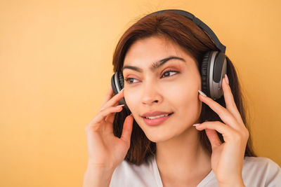 Close-up of smiling young woman wearing headphone against colored background